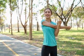Young woman stretching her arms on a park path, preparing for an outdoor workout. Fitness and healthy lifestyles concept.