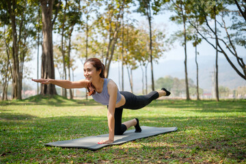 Fototapeta premium Young woman practicing yoga on mat in a serene park, Wellness, mental health and healthy lifestyle concept.