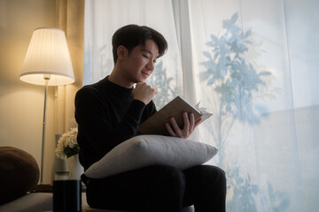 Relaxed man in a black sweater sitting comfortably in a warm, softly lit living room and reading a notebook.