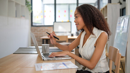 Young professional woman reviews documents while typing on her laptop.