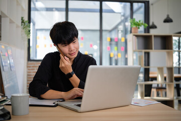 Confident young businessman talking on his smartphone while working on a laptop in an office.