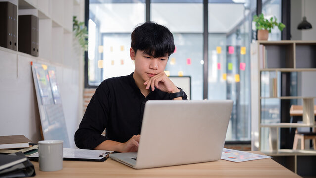 man sits at a wooden desk, engaged with her laptop while enjoying a coffee break in a trendy co-working space - Powered by Adobe