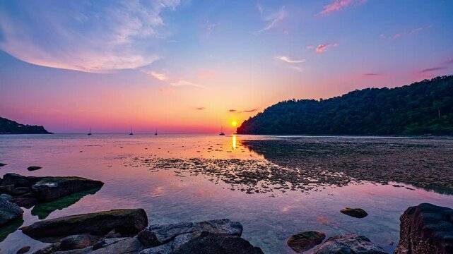 Time lapse The sun sets at the tip of Ao Mai Ngam, Surin Islands. The reflection of the setting sun.while the silhouette of lush green hills and anchored sailboats enhance the peaceful ambiance.