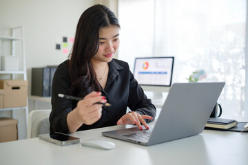Focused young businesswoman holding pen working with laptop in modern office.