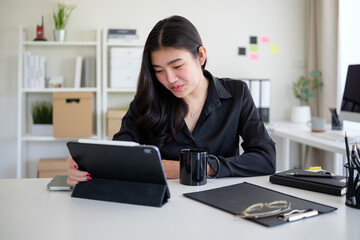 Businesswoman in a black blouse is focused on her tablet, working in a stylish and organized office space.