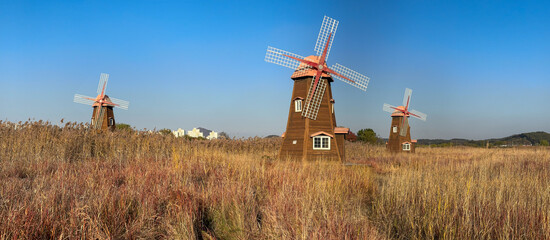 Three Wooden Windmills in a Golden Field Under a Clear Blue Sky
