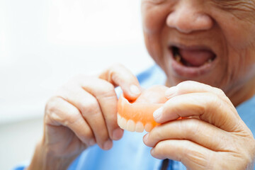 Asian senior woman patient wearing teeth denture into her mouth for chew food.