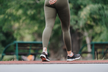 A person in green leggings and black running shoes walking outdoors on a pathway in a park during...