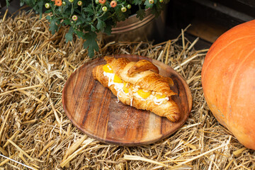 Sweet croissant with peach, walnuts and cream cheese on a wooden plate, rustic setting with straw and pumpkin background