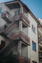 Exterior view of a residential building showcasing its concrete staircase adorned with red banisters, and light grey walls against a clear blue sky.