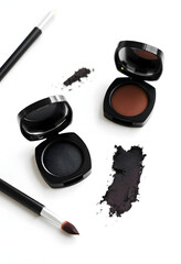 Dark makeup shadows placed on a white table, showcasing an elegant and dramatic beauty setup. The rich, deep hues of the eyeshadow provide a striking contrast against the clean white surface.


