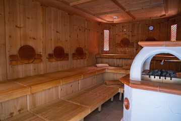 Cozy sauna interior with light wood paneling, circular backrests, lattice windows, and a white dome shaped stove in Ischgl ski resort, Austria. © Aerial Film Studio