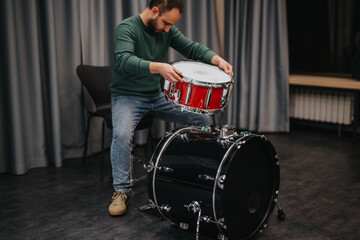 A man carefully assembles a drum set in a music studio, preparing for practice. The scene captures...