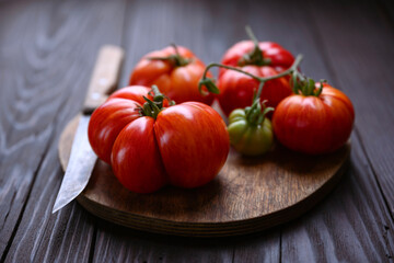 Ripe red tomatoes with knife on wooden cutting board on rustic table close up. Food photography