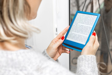 woman reading e-book standing near window in house. girl reading e-book at home. female hand holding an e-book. ebook mockup. place for inscription. man using e-book