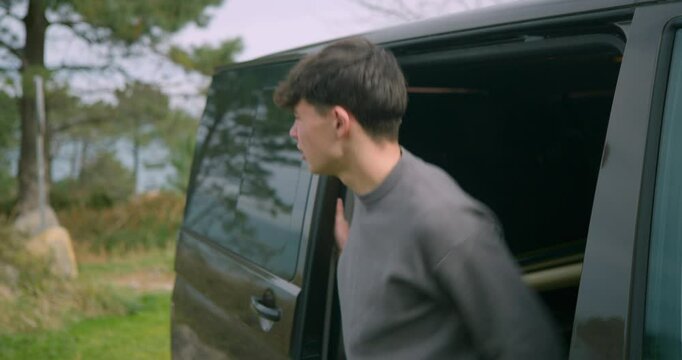 The boy opens the back door of the van and gets out. He looks around.