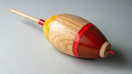 Handcrafted wooden fishing float in minimalist style with red and yellow accents on grey background used for angling equipment or tackle concepts