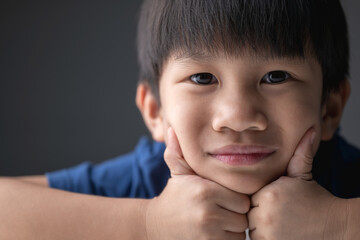 Close-up portrait of a cheerful young boy resting his chin on his hands with a soft smile.