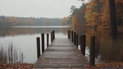 Obraz premium A rustic wooden pier extending into a peaceful lake, surrounded by autumn foliage, capturing the beauty of nature tourism.