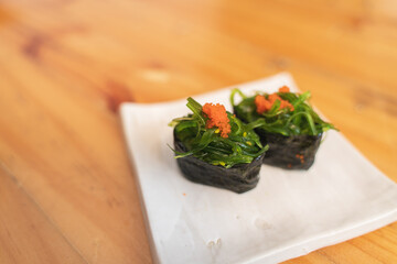 Two pieces of seaweed salad sushi, topped with orange roe, served on a ceramic plate.