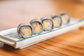 Five sushi rolls with fish, egg, and rice served on a ceramic tray.