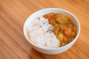 White rice with black sesame seeds and vegetable curry in a bowl on a wooden surface