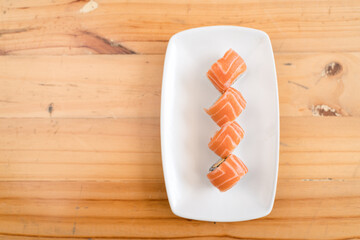 Fresh salmon sushi rolls neatly arranged on a white plate with a wooden table background.