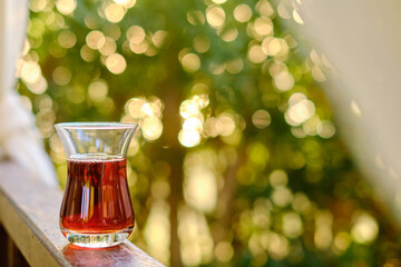 Glass of tea resting on wooden balcony, sunlight filtering through lush green leaves, creating warm and peaceful atmosphere of relaxation and serenity