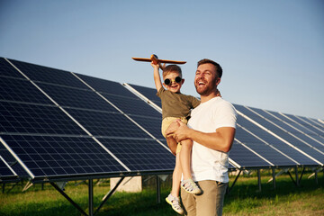 Toy plane in hand. Father with his little son are together near the solar panels