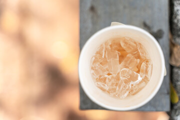 Top view of a disposable cup filled with clear ice cubes, placed on a textured surface with a...