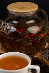 red rosehip fruits and hot green tea in a transparent teapot