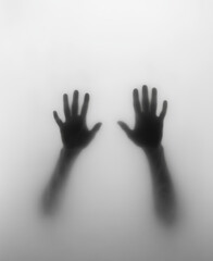 Shadow of hands behind frosted glass with eerie mysterious atmosphere creating trapped feeling