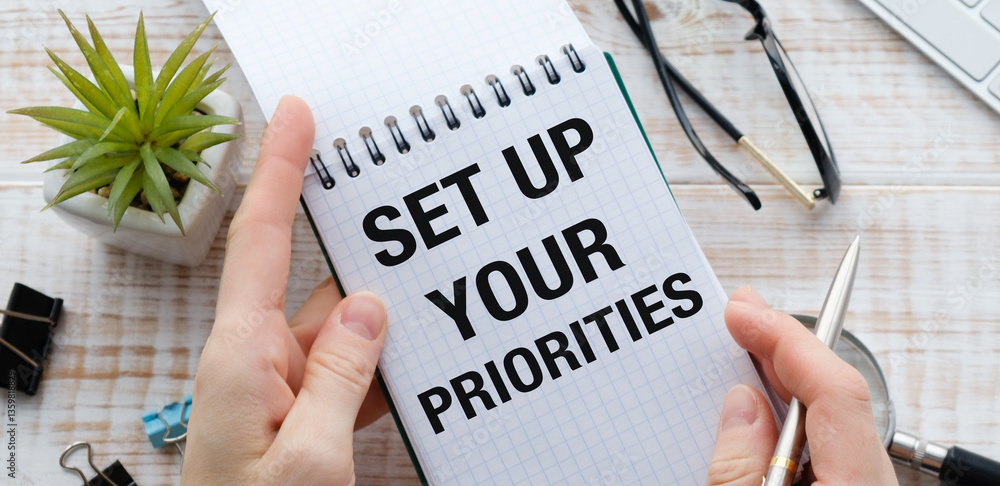 Poster a person is holding a notebook with the words set up your priorities written on it.