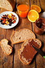 Spreading chocolate cream on whole wheat bread for breakfast with orange juice and dried fruit