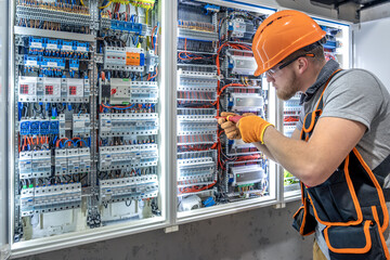 Male electrician working in electrical panel. Male electrician in overalls.