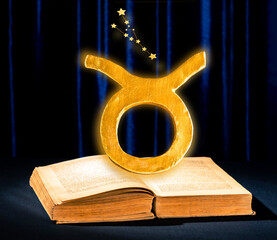 Golden zodiac sign Taurus above old astrology book against blue velvet curtain