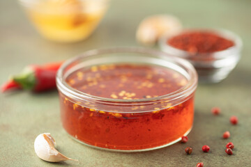 Hot honey in bowl and  chili peppers on green background.