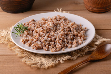 Cooked buckwheat served on a white plate with fresh herbs on a rustic wooden table