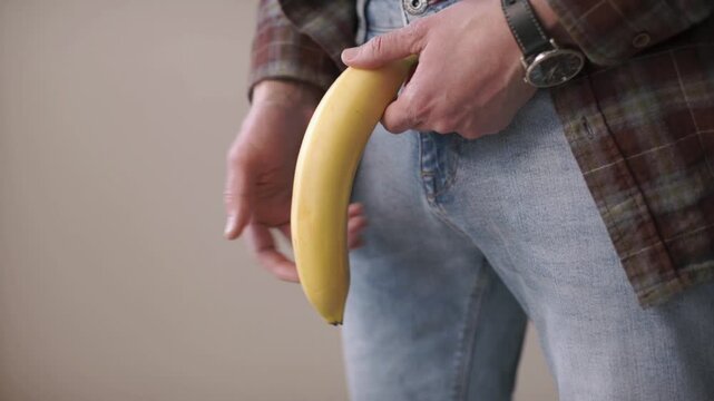 a man holds a banana in the groin area. Problems with the prostate. Age intimate problems of men. Steroids and potency. Passive lifestyle