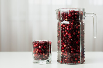 Cranberry. Small forest red berry. Cranberries in a jug and in a glass on the table. A glass of cranberries. Vitamins from nature. Selective focus.