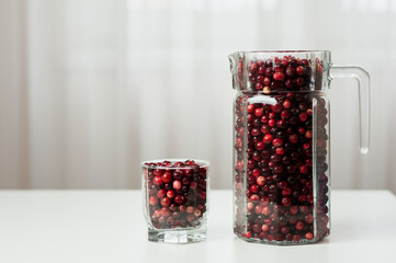 Cranberry. Small forest red berry. Cranberries in a jug and in a glass on the table. A glass of cranberries. Vitamins from nature. Selective focus.