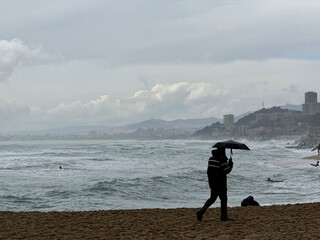 Lonely figure with Umbrella on the Stormy Beach. A solitary person holding an umbrella stands on...