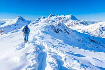 Skier traversing snowy mountain ridge, sunny winter landscape, adventure