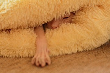 A hairless Sphynx cat is sleeping under a soft, plush blanket, with one paw reaching out. Cozy and heartwarming scene.
