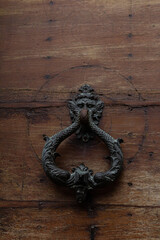Rustic brown wooden door with a round vintage metal knocker, rich in texture and history.
