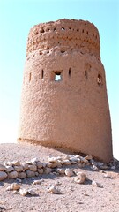 Weathered mud stone watchtower rising from arid desert ground, silhouetted against pristine azure...