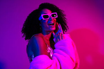 Young stylish woman in violet neon lighting posing confidently during a club photoshoot, showcasing her vibrant expression
