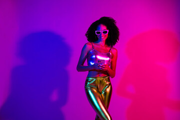 Young fashionable woman in a glamorous outfit smiling confidently under vibrant neon lights with ultraviolet colors