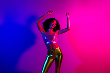 Young woman dancing joyfully in glowing neon lights wearing stylish metallic outfit, displaying vibrant energy