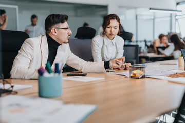 A diverse group of people work together in a modern office. Focus is on two employees discussing ideas, showcasing teamwork, collaboration, and multicultural dynamics in a business environment.